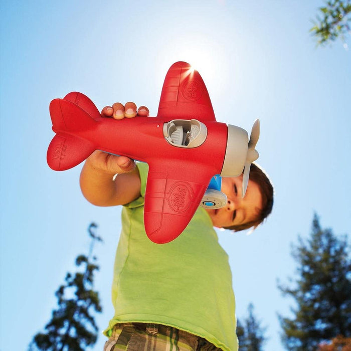 Red toy airplane with grey propeller and wheels held up against a bright blue sunny sky.