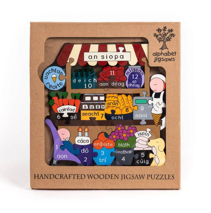 Colorful wooden jigsaw in a brown box showing a shop scene with Irish numbers 1-12 and words on shaped pieces.