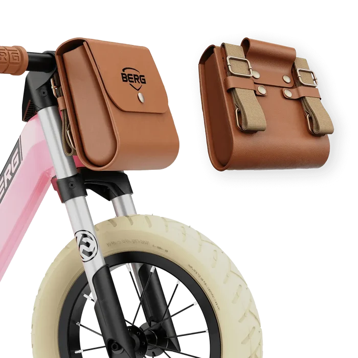 Close-up of a pink balance bike with a brown leather bag, silver front fork, and white tire.