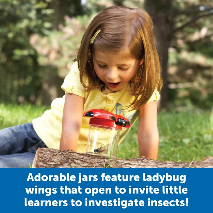 A child looks into a clear bug jar with a red ladybug lid, magnifying an insect inside while sitting outdoors.