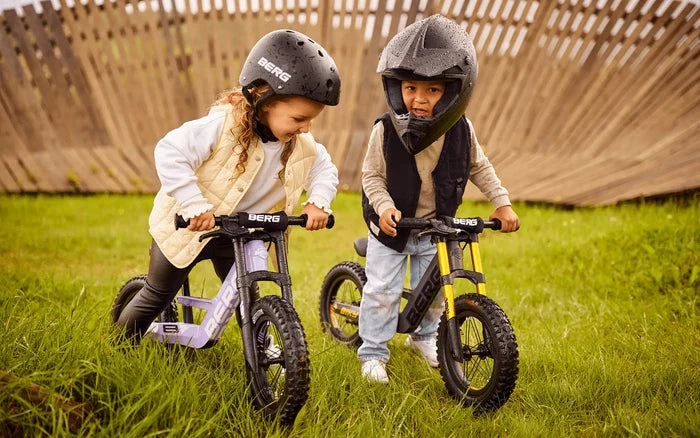 Two children on balance bikes; the purple Biky Cross features knobby off-road tires and a handbrake.