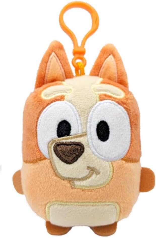Small orange and cream plush dog keychain with large white eyes and a brown nose, featuring an orange plastic clip on top.