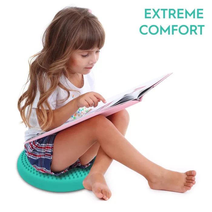 Girl sits on a round teal spiked sensory cushion while reading a book. Text says EXTREME COMFORT.