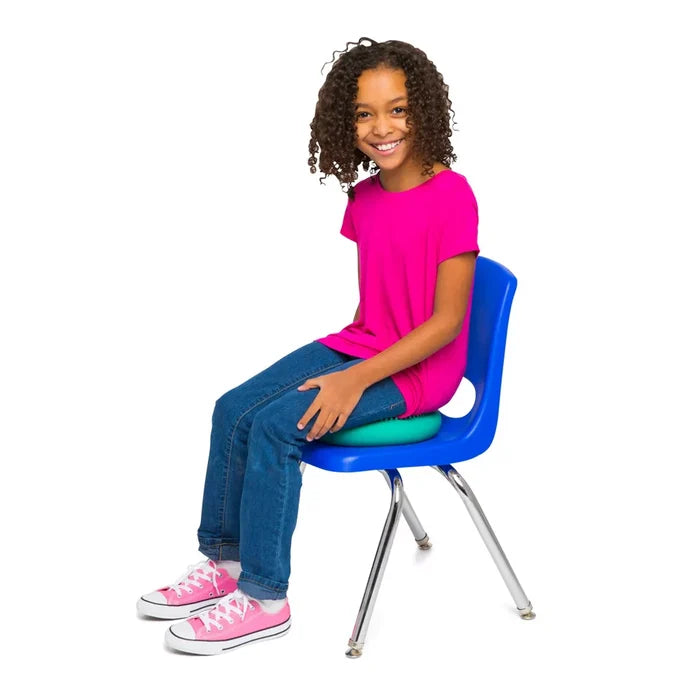 Smiling girl sits on a blue chair using a teal, round inflatable sensory wiggle cushion on the seat.