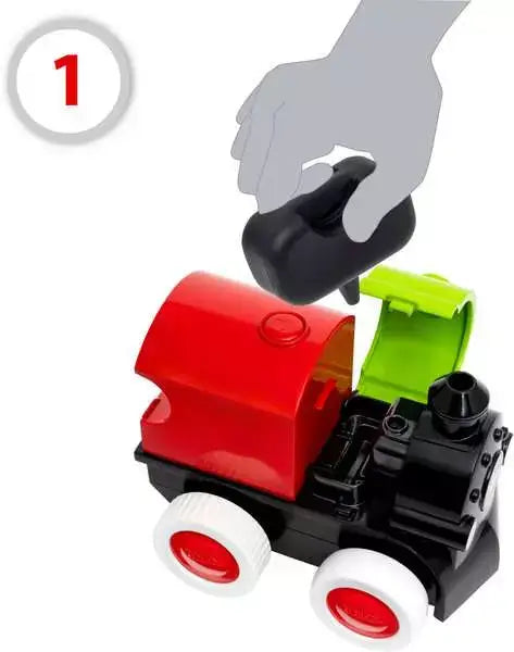 Hand inserting a black water tank into a red and black toy train with an open green lid and white wheels.