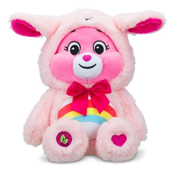 Sitting pink plush bear in a light pink bunny hoodie with floppy ears, a magenta bow, and a rainbow belly.
