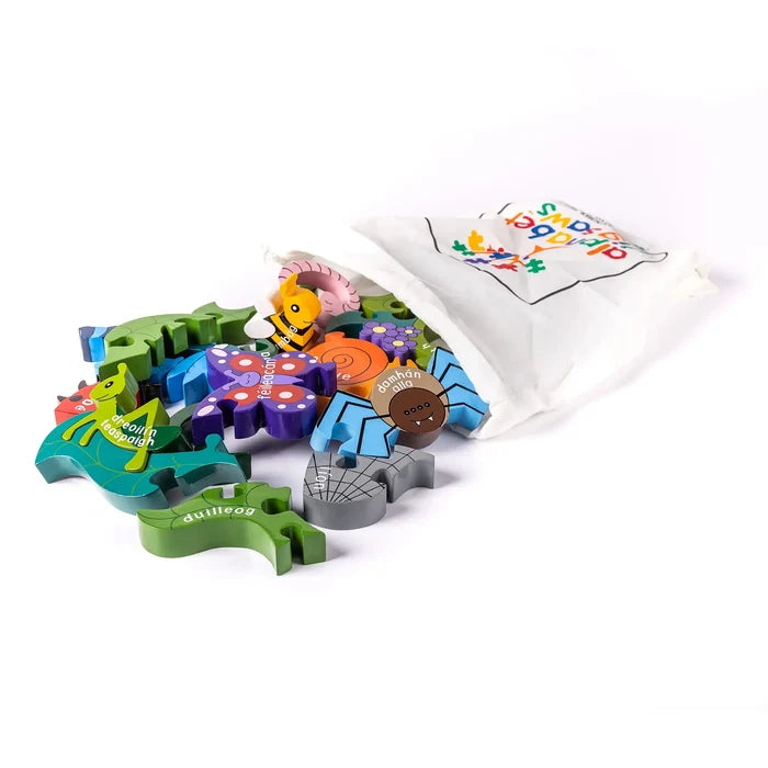 Brightly colored wooden bug puzzle pieces with Irish words spilling from a white drawstring bag.