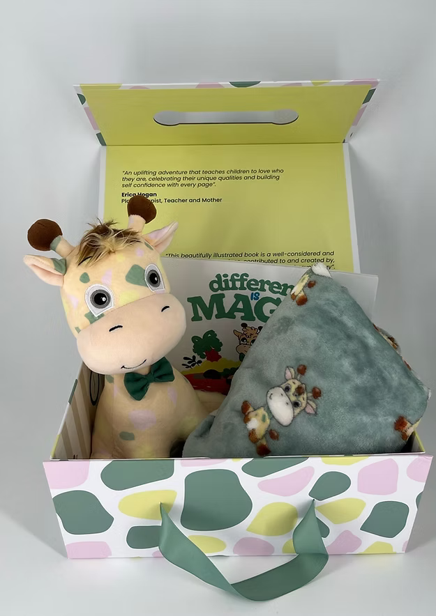 Spotted gift box holding a yellow plush giraffe with a green bow tie, a picture book, and a soft green fleece blanket.