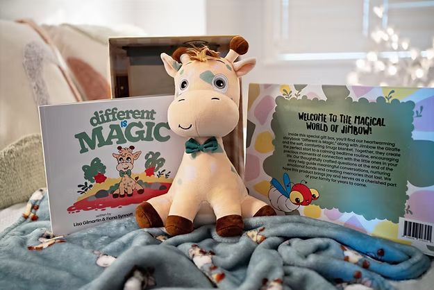Plush giraffe with a teal bowtie, a children's book, and a blue patterned blanket displayed in a decorative gift box.