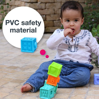 Toddler plays with colorful, textured blocks including a stack of green, orange, and teal ones on a tiled patio.