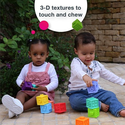 Two toddlers play outdoors with colorful soft 3D textured blocks. Text says 3-D textures to touch and chew.