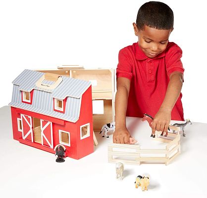 Young boy playing with a red and white wooden toy barn, fence, and various plastic farm animal figurines.