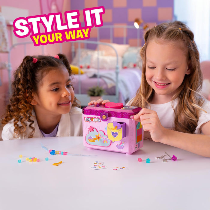 Two girls customize a pink and purple glittery jewelry box with stickers and beads on a white table.