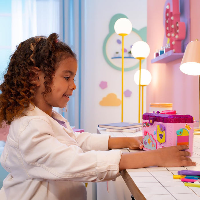 A young girl playing with a pink and purple glittery jewelry box decorated with colorful stickers.