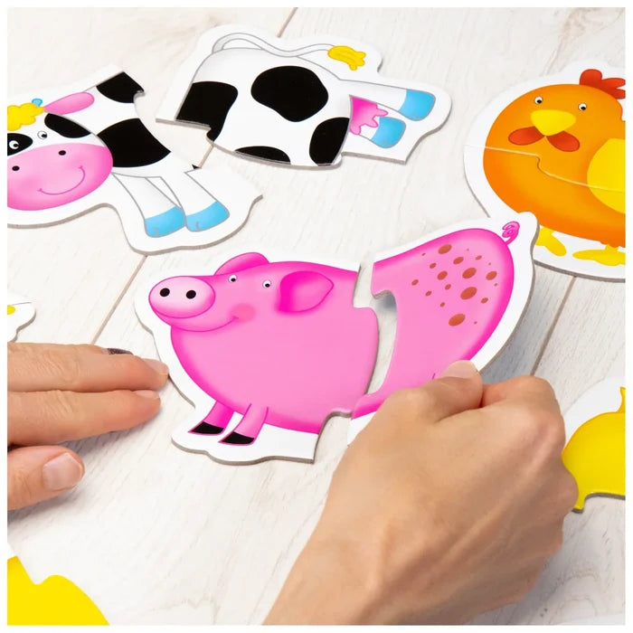Hands joining two pieces of a pink pig puzzle next to cow and chicken puzzles on a light wood surface.