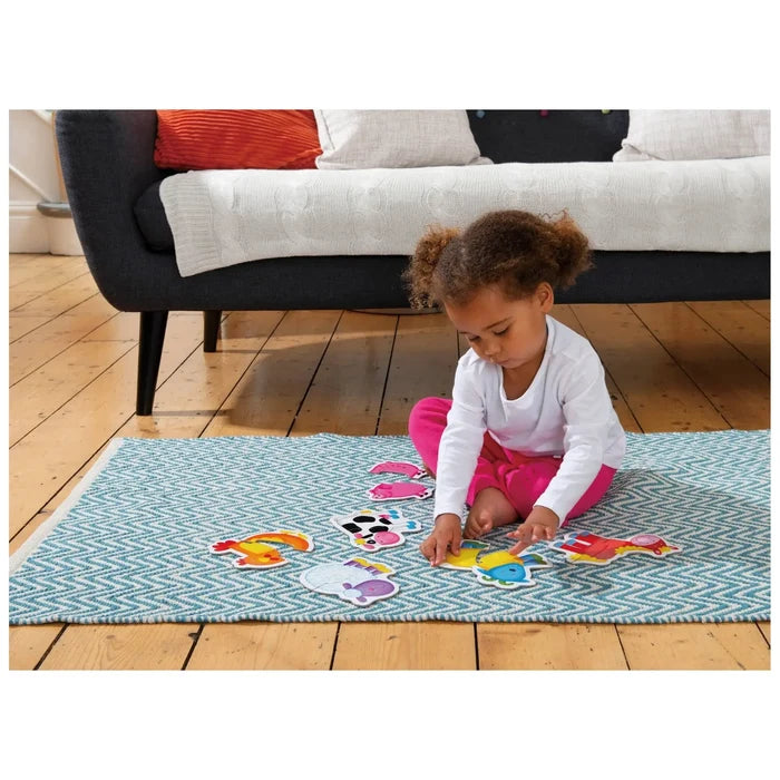 Toddler girl playing with colorful two-piece farm animal puzzles on a blue patterned rug.