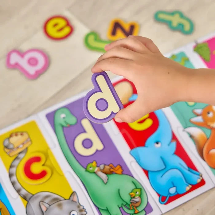 Child’s hand placing a purple letter ‘d’ piece into a colorful alphabet puzzle board with animal illustrations.
