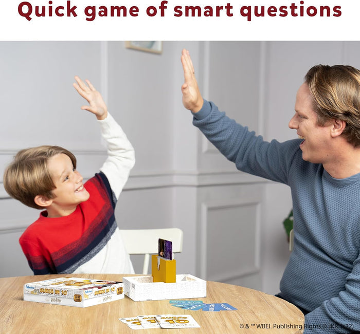 Man and boy high-five over a yellow card stand, cards, and the Harry Potter Guess in 10 box on a round wooden table.