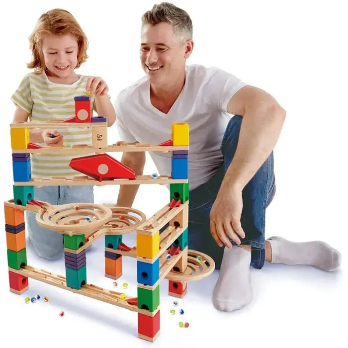 A man and child play with a multi-level wooden marble run featuring vibrant blocks, tracks, and spiral funnels.