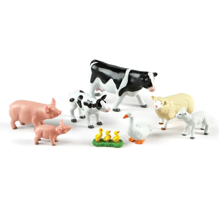Plastic toy farm animal families: pink pigs, black and white cows, beige sheep, and a white goose with yellow goslings.