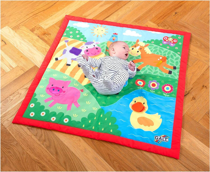 Baby lying on a colorful square farm-themed playmat with illustrations of a pig, duck, cow, and horse.
