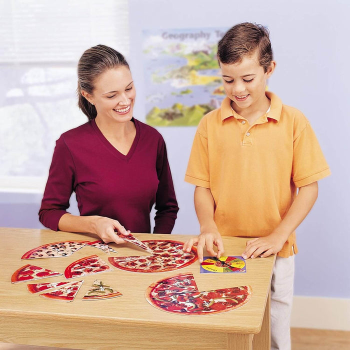 Woman and boy play with realistic cardboard pizza slices showing various fractions and a colorful game spinner.