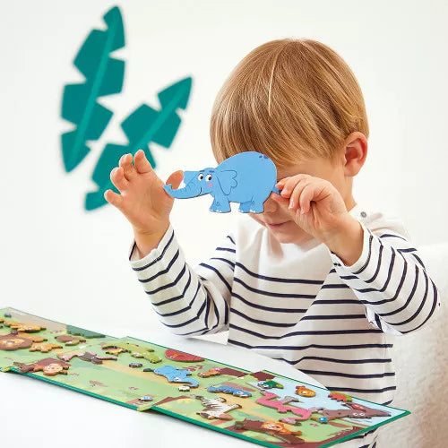 A child holds a blue elephant magnet to his eye while playing with a colorful fold-out magnetic animal scene.