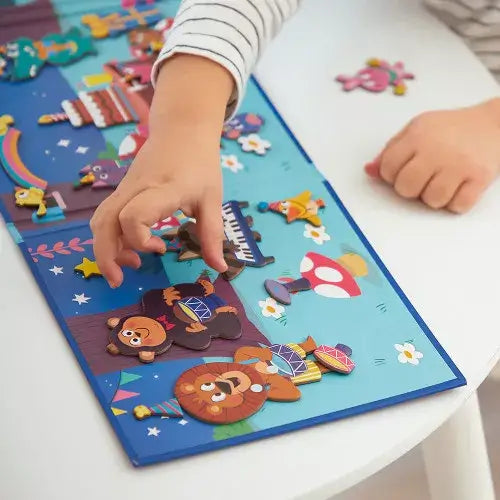 Child's hands move colorful magnets of drumming animals on a vibrant blue and green illustrated storybook scene.