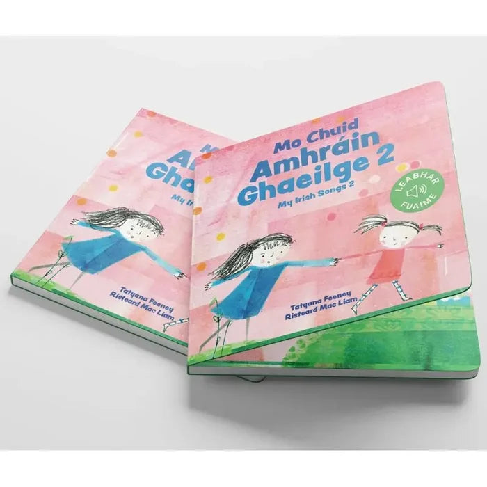 Two pink Irish children's board books with simple illustrations of girls dancing on a grassy hill under a pink sky.