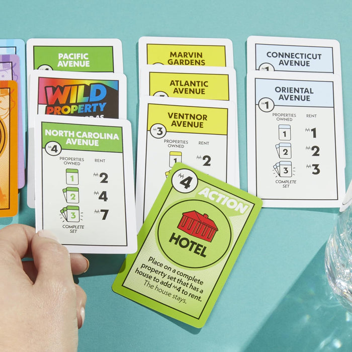 Hand holding a green property card over several colorful game cards on a bright teal surface.