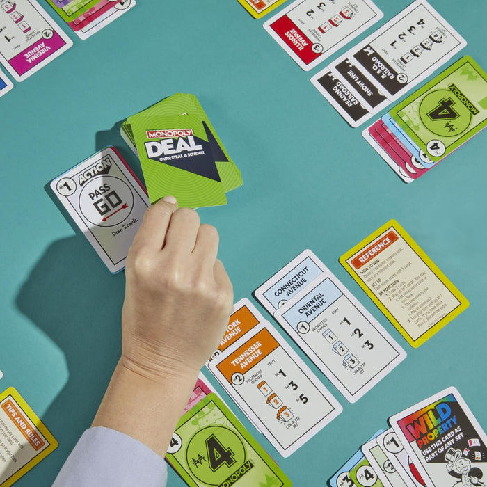 A hand draws a card from a green deck among colorful property and action cards spread across a teal surface.
