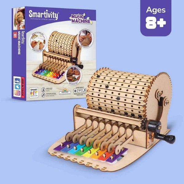 Assembled wooden music machine kit with hand-cranked cylinder and rainbow xylophone keys next to purple retail packaging.