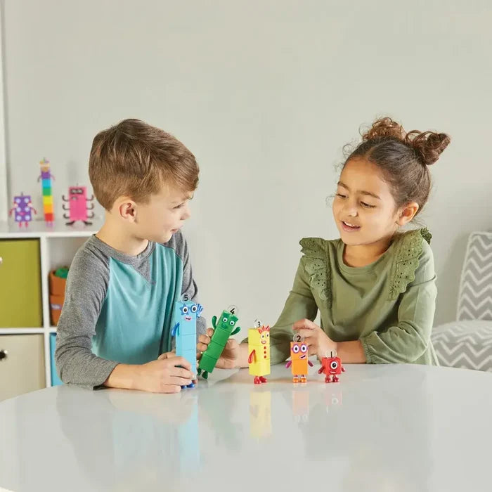 Two children play with five colorful, numbered block characters of different heights on a white table.