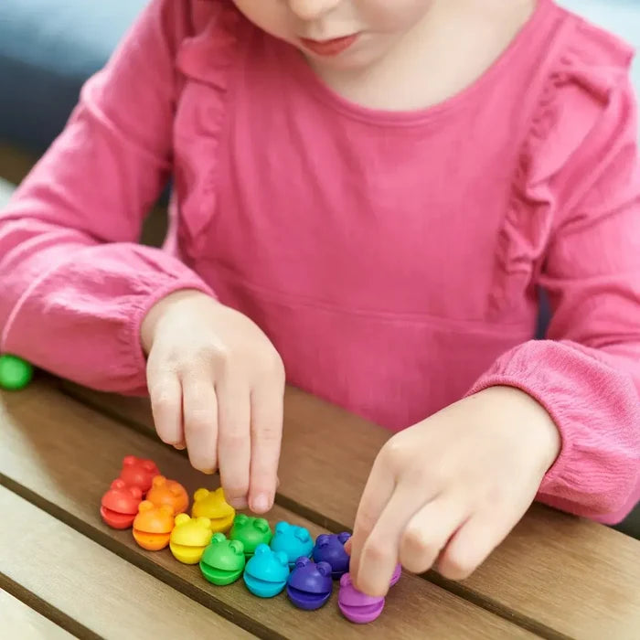Child arranging small, colorful spherical Numberblob counters in a rainbow row on a wooden table.