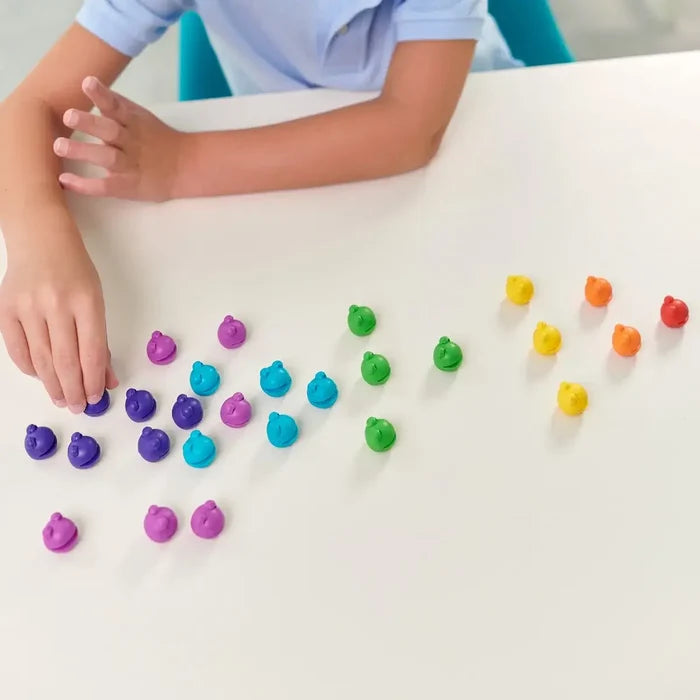 Child sorting small, colorful character counters with faces into color groups on a white table.