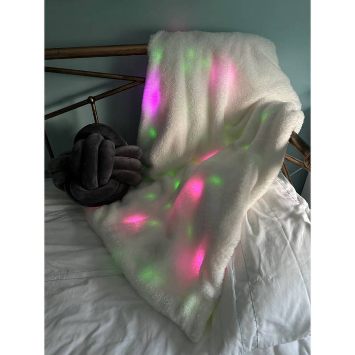 White shaggy throw blanket with internal pink and green glowing lights, draped over a bed headboard.