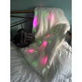 White shaggy throw blanket with internal pink and green glowing lights, draped over a bed headboard.