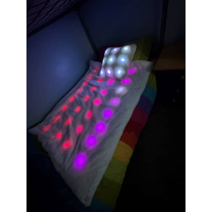 White plush blanket and pillow on a bed, glowing with pink, purple, and white circular LED lights in a dark room.
