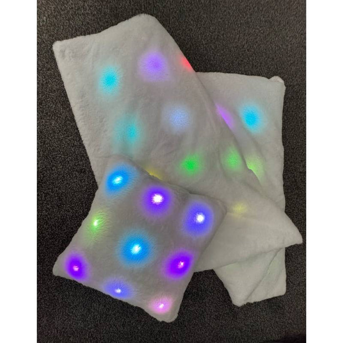 White plush blanket and square pillow featuring glowing multi-colored LED lights embedded in the soft fuzzy fabric.