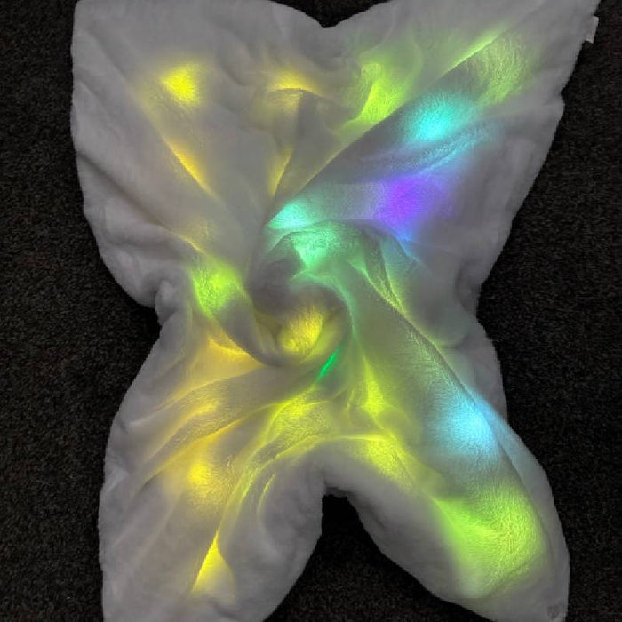 Soft white plush blanket with glowing yellow, green, and blue internal lights, bunched in a star shape.