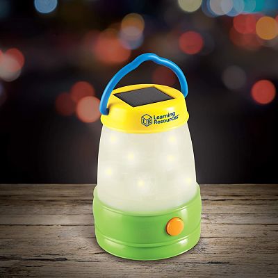 Kids' toy lantern with blue handle, yellow top with solar panel, and glowing white center on a wooden table.