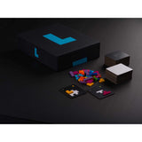 Black game box with a vibrant blue L, colorful puzzle pieces, and stacks of cards on a dark background.