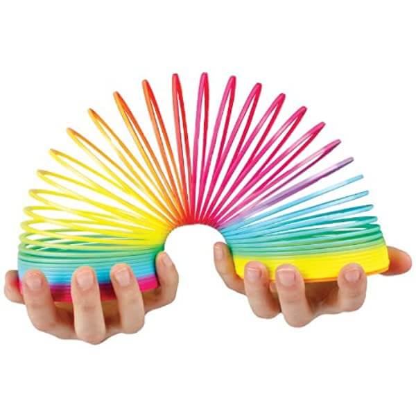 Hands holding a vibrant, multicolored plastic spring toy arched into a rainbow shape.