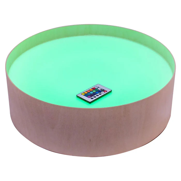 Round light-wood table with an illuminated neon green top surface and a small remote control.