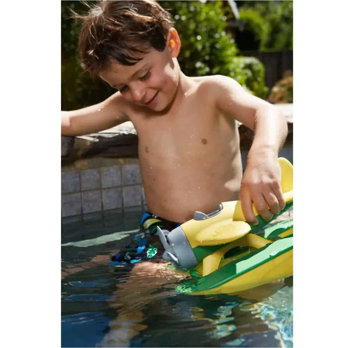 Boy playing in a pool with a yellow and green toy seaplane featuring grey nose and propeller details.
