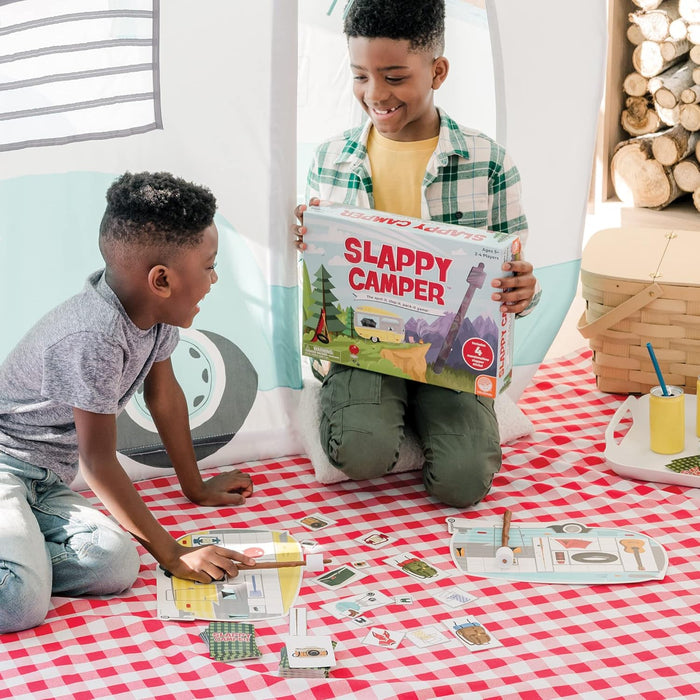 Two boys playing a camping board game with marshmallow sticks and camper cards on a red checkered picnic blanket.
