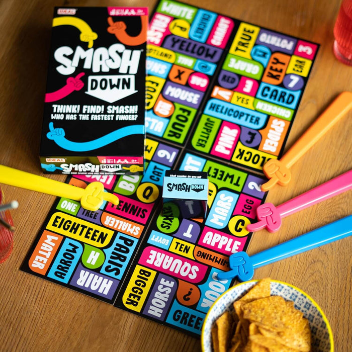 Smash Down board game with a colorful word grid, four finger-pointing smashers, and a game die on a wooden table.