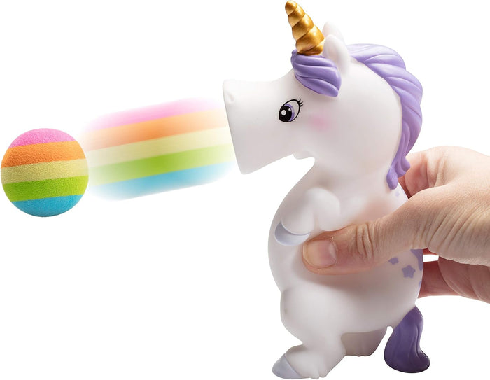 Hand squeezes a white unicorn toy with a purple mane and gold horn, firing a rainbow foam ball from its mouth.