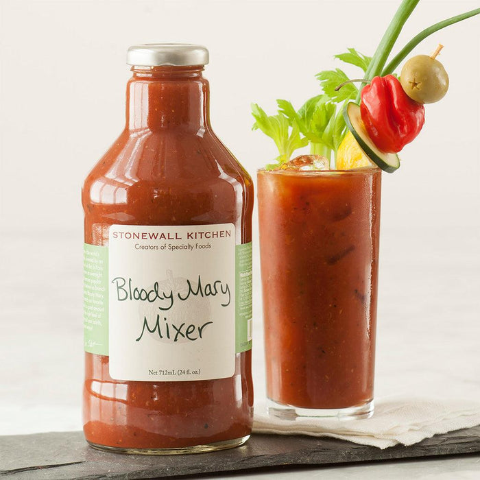 "Stonewall Kitchen Bloody Mary Mixer bottle with garnished drink – Glass bottle of Bloody Mary Mixer alongside a tall glass filled with the cocktail, garnished with celery, cucumber, pepper, and olive."