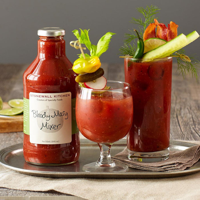 "Stonewall Kitchen Bloody Mary Mixer with two garnished drinks – Bottle of Bloody Mary Mixer on a serving tray with two prepared cocktails, garnished with celery, cucumber, radish, pickles, and peppers."